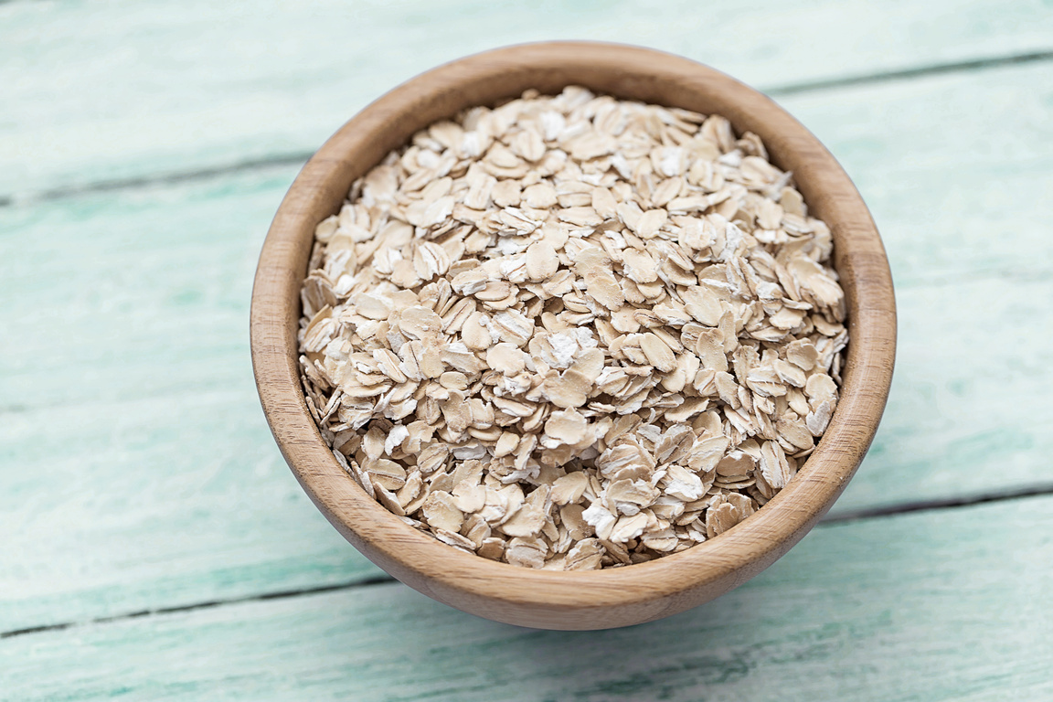 Raw Oatmeal or Oat Flakes in a Wooden Bowl on a Blue Wooden Background